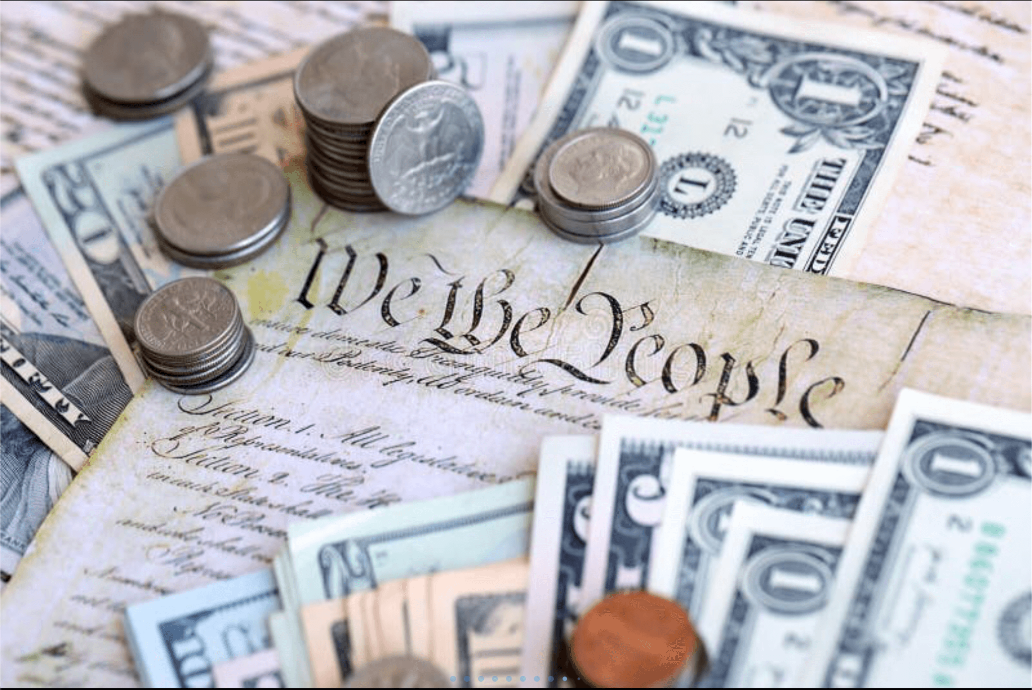 US currency and coins scattered over the "We the People" preamble of the Constitution.